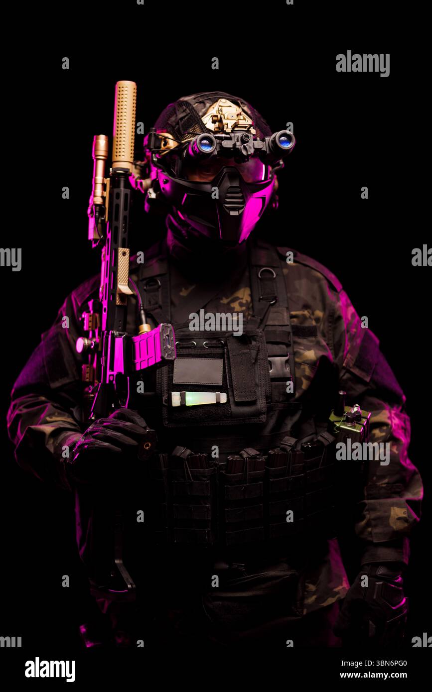 Eine taktische Person, die Tarnung trägt und mit einer Nachtsichtbrille und einem Gewehr ausgestattet ist, beleuchtet durch leuchtendes Neonlicht in lila, was eine M Stockfoto