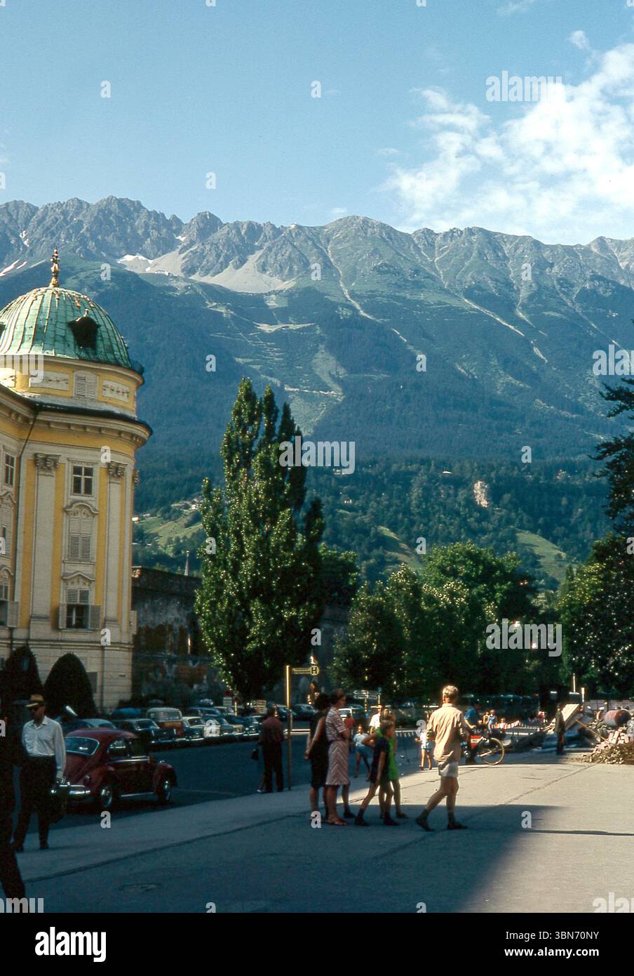 Österreich der 1960er Jahre - Menschen, die an der Habsburger Hofburg, Innsbruck, Rennweg im Jahr 1967 vorbeilaufen - mit den Tiroler Alpen im Hintergrund Stockfoto