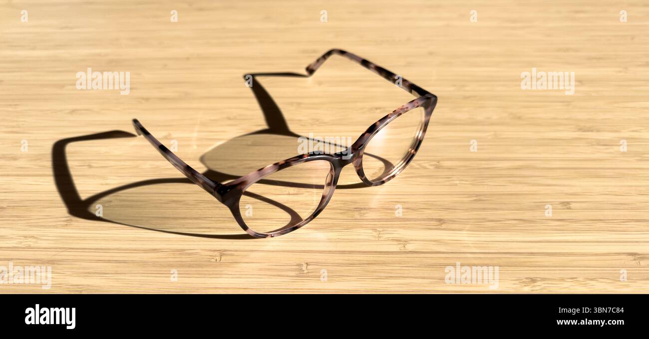 Moderne Brille in kontraststarker Beleuchtung auf Holztisch mit Kopierraum Stockfoto