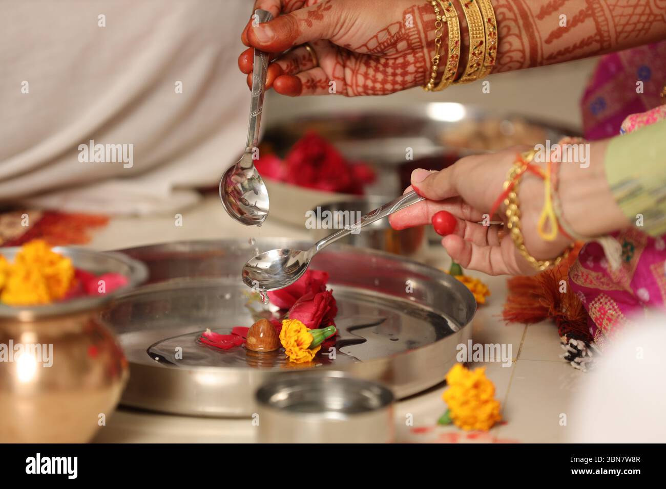 Eine Nahaufnahme eines hinduistischen Hochzeitsrituals mit einem Weihwasseropfer (Abhishekam oder Achamanam). Zwei Hände (eine männliche, eine weibliche) halten Löffel Stockfoto