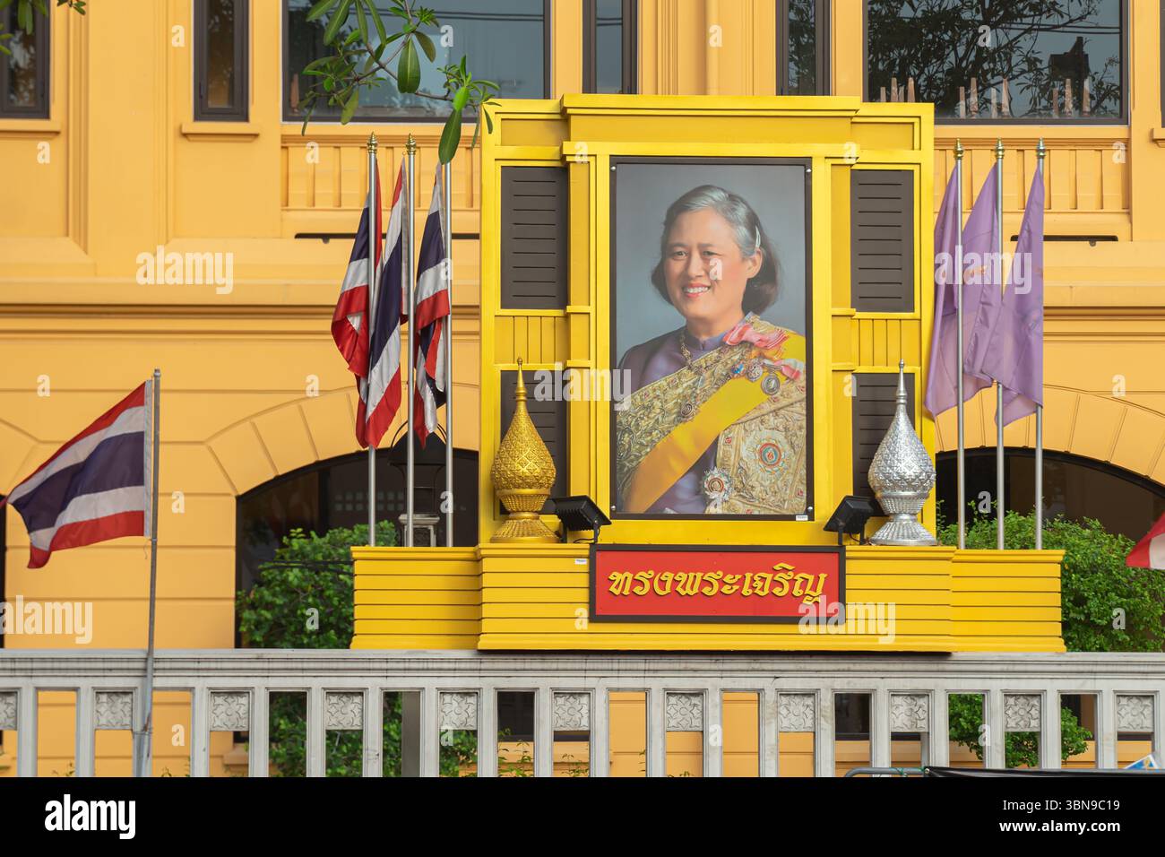 Ein Porträt der Königin Sirikit von Thailand ist mit thailändischen Flaggen und anderen Symbolen vor dem Regierungsgebäude in bangkok ausgestellt Stockfoto