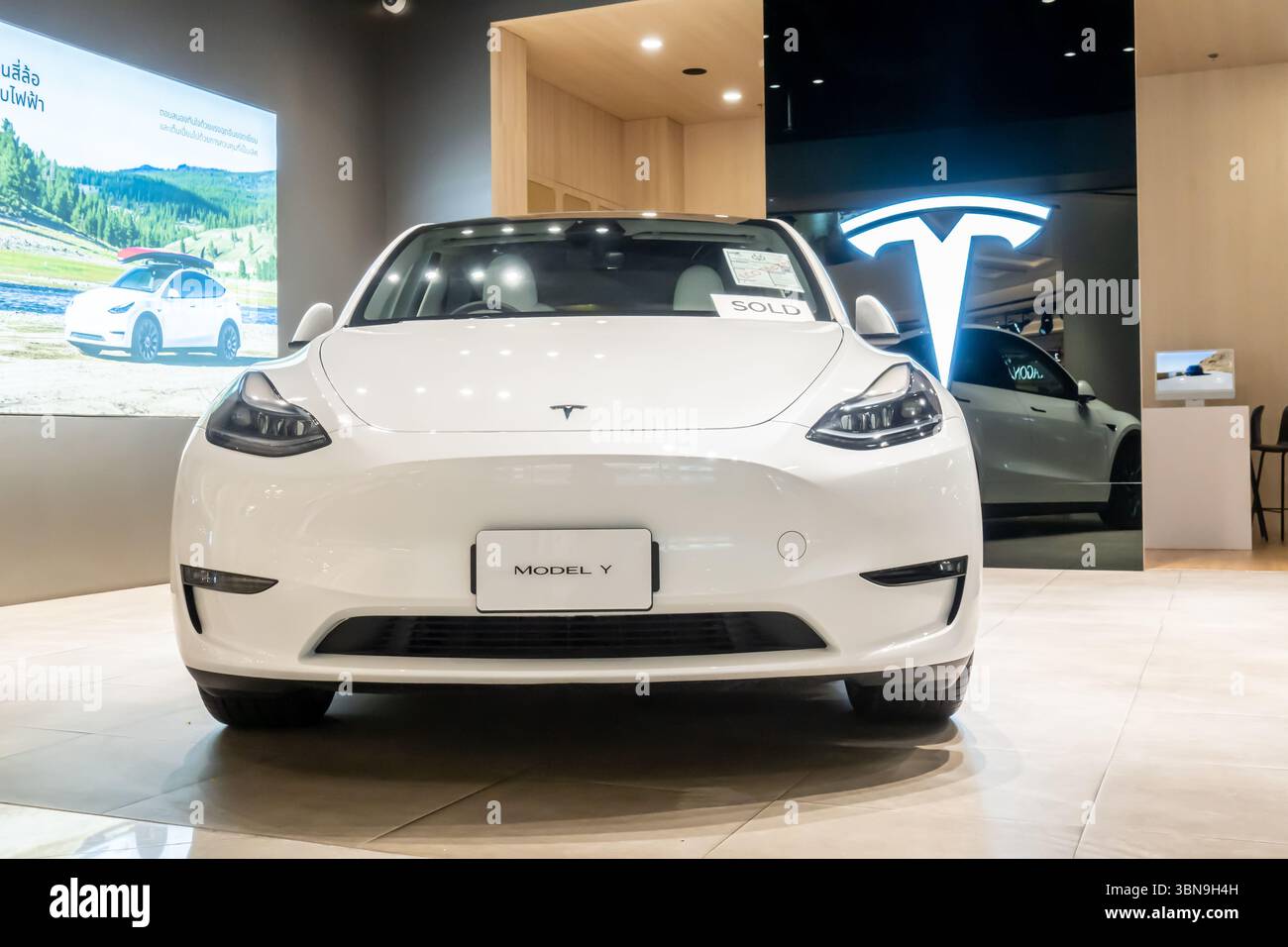 2025 Tesla Modell Y wird in einem Ausstellungsraum ausgestellt, Vorderansicht, tesla-Logo im Hintergrund Stockfoto