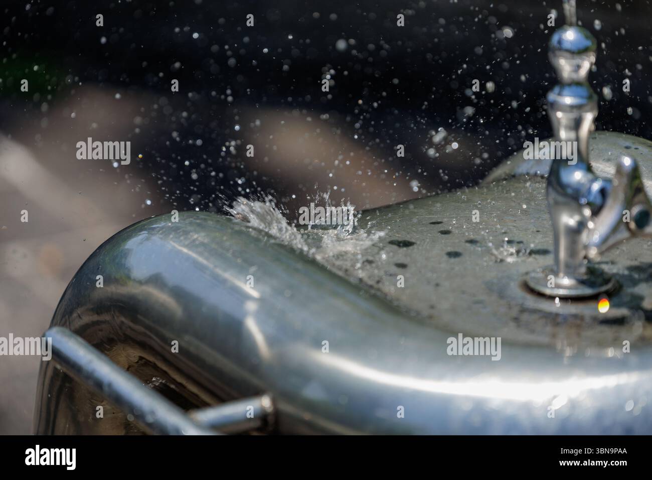 Fallende Tropfen explodieren beim Aufprall auf das Edelstahlbecken des Trinkbrunnens. Tropfen in der Mitte der Luft sorgen für dynamische und erfrischende Qualität. Stockfoto