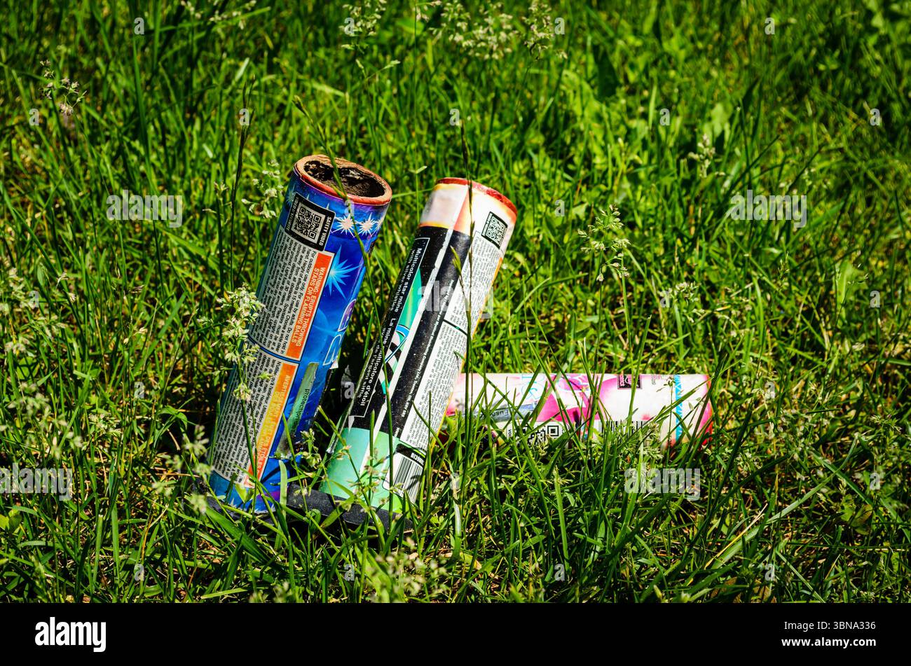 Nahaufnahme von drei gebrauchten Feuerwerkskannistern im Gras an einem sonnigen Tag Stockfoto