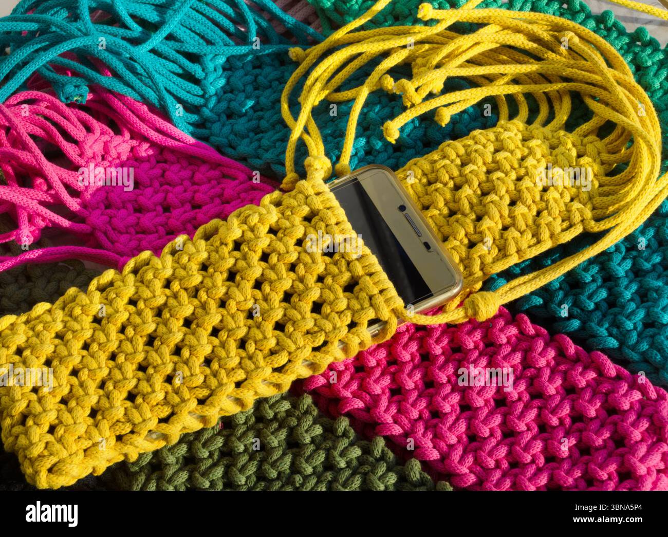 Eine lebendige Nahaufnahme handgestrickter Macramé-Smartphone-Taschen. Eine Kollektion handgefertigter Accessoires in Türkis, Fuchsia, Oliven und Gelb Stockfoto