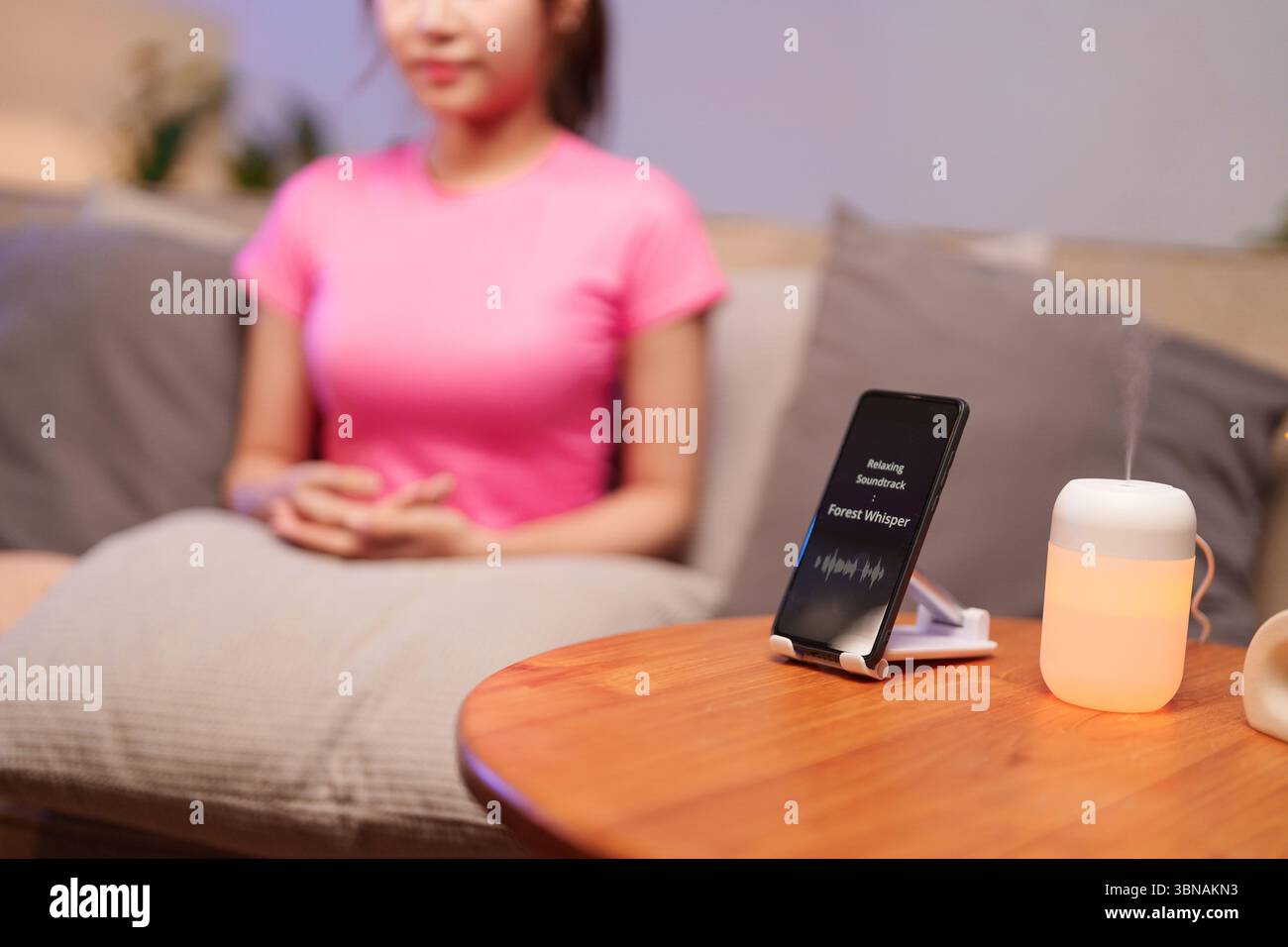 Genießen Sie Ruhe mit Aromatherapie-Diffusor und Klangtherapie, die auf einem Smartphone abgespielt wird. Entdecken Sie die asiatische Wellness-Routine für Erwachsene Frauen für Relaxatio Stockfoto