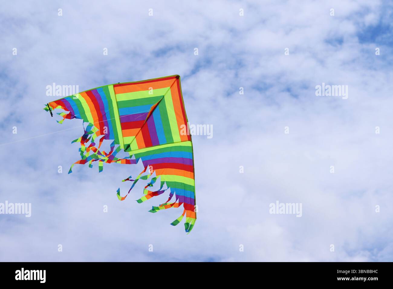 Heller Drachen vor dem bewölkten Himmel. Spielzeug für Kinder und Erwachsene. Outdoor-Aktivitäten. Bunte Drachenfliegen am Himmel, windiges Wetter. Wolkenlose Stimmung Stockfoto