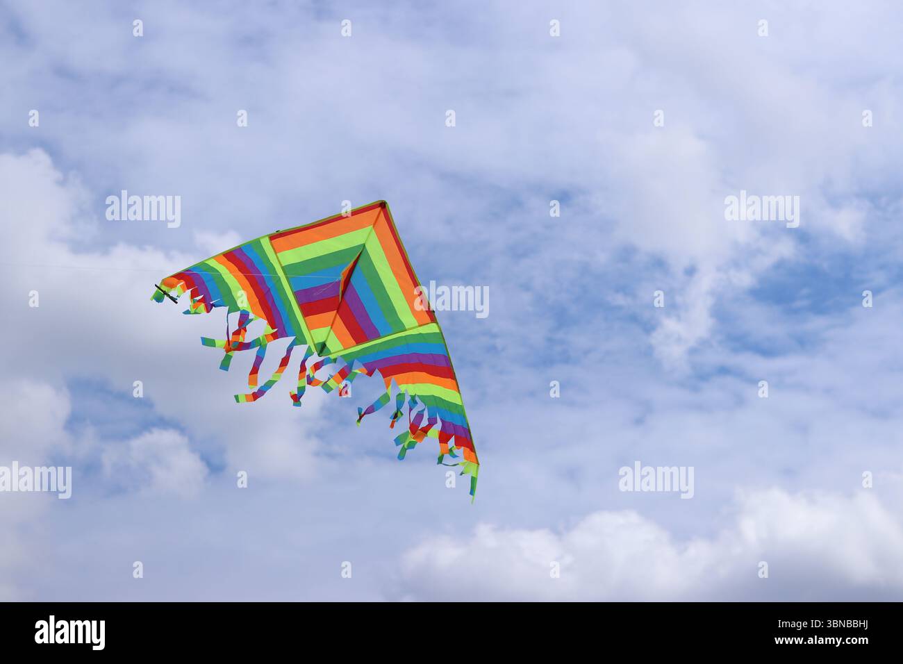 Heller Drachen vor dem bewölkten Himmel. Spielzeug für Kinder und Erwachsene. Outdoor-Aktivitäten. Bunte Drachenfliegen am Himmel, windiges Wetter. Wolkenlose Stimmung Stockfoto