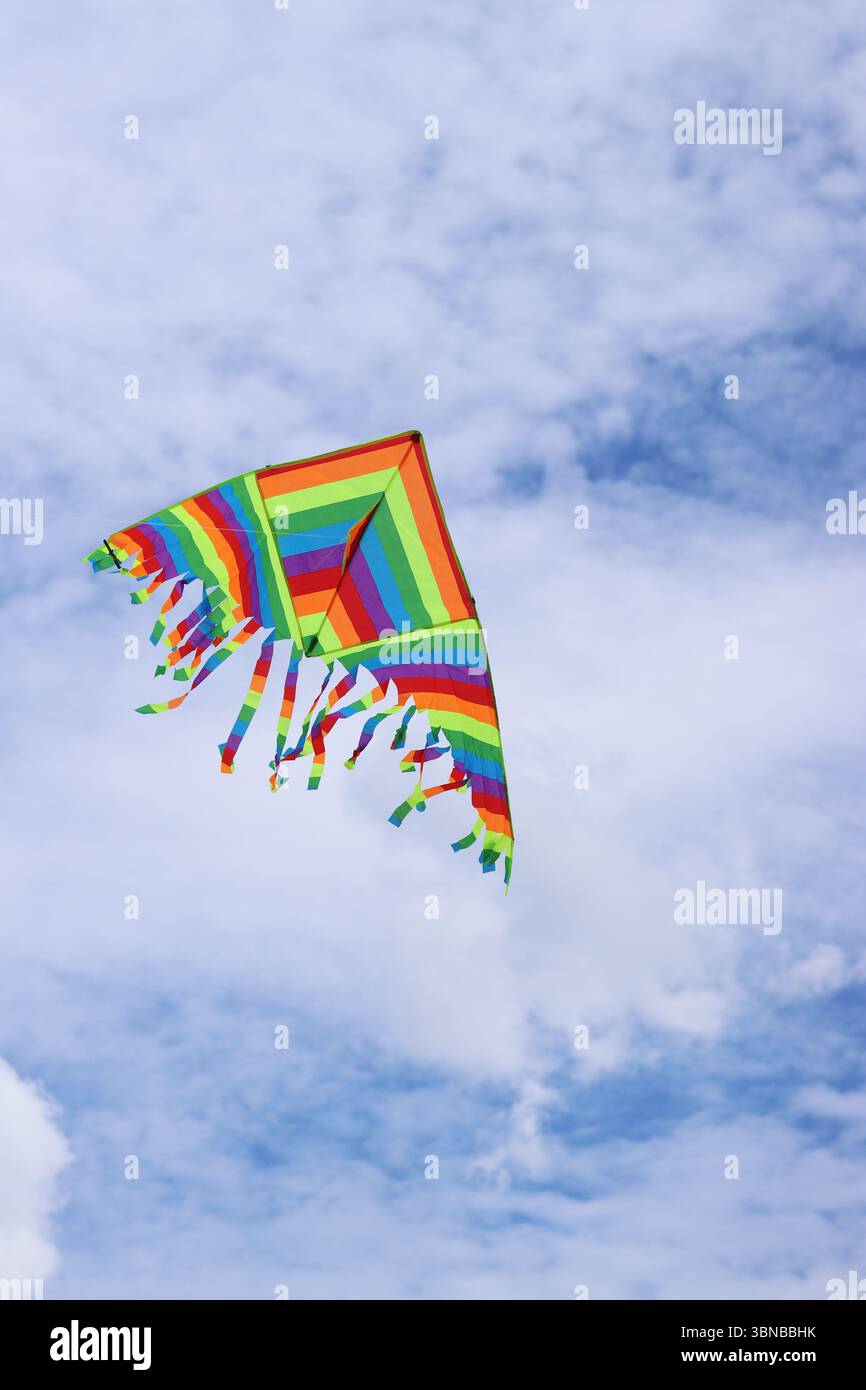 Heller Drachen vor dem bewölkten Himmel. Spielzeug für Kinder und Erwachsene. Outdoor-Aktivitäten. Bunte Drachenfliegen am Himmel, windiges Wetter. Wolkenlose Stimmung Stockfoto