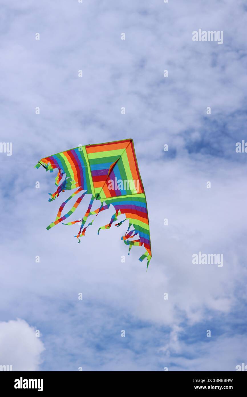 Heller Drachen vor dem bewölkten Himmel. Spielzeug für Kinder und Erwachsene. Outdoor-Aktivitäten. Bunte Drachenfliegen am Himmel, windiges Wetter. Wolkenlose Stimmung Stockfoto