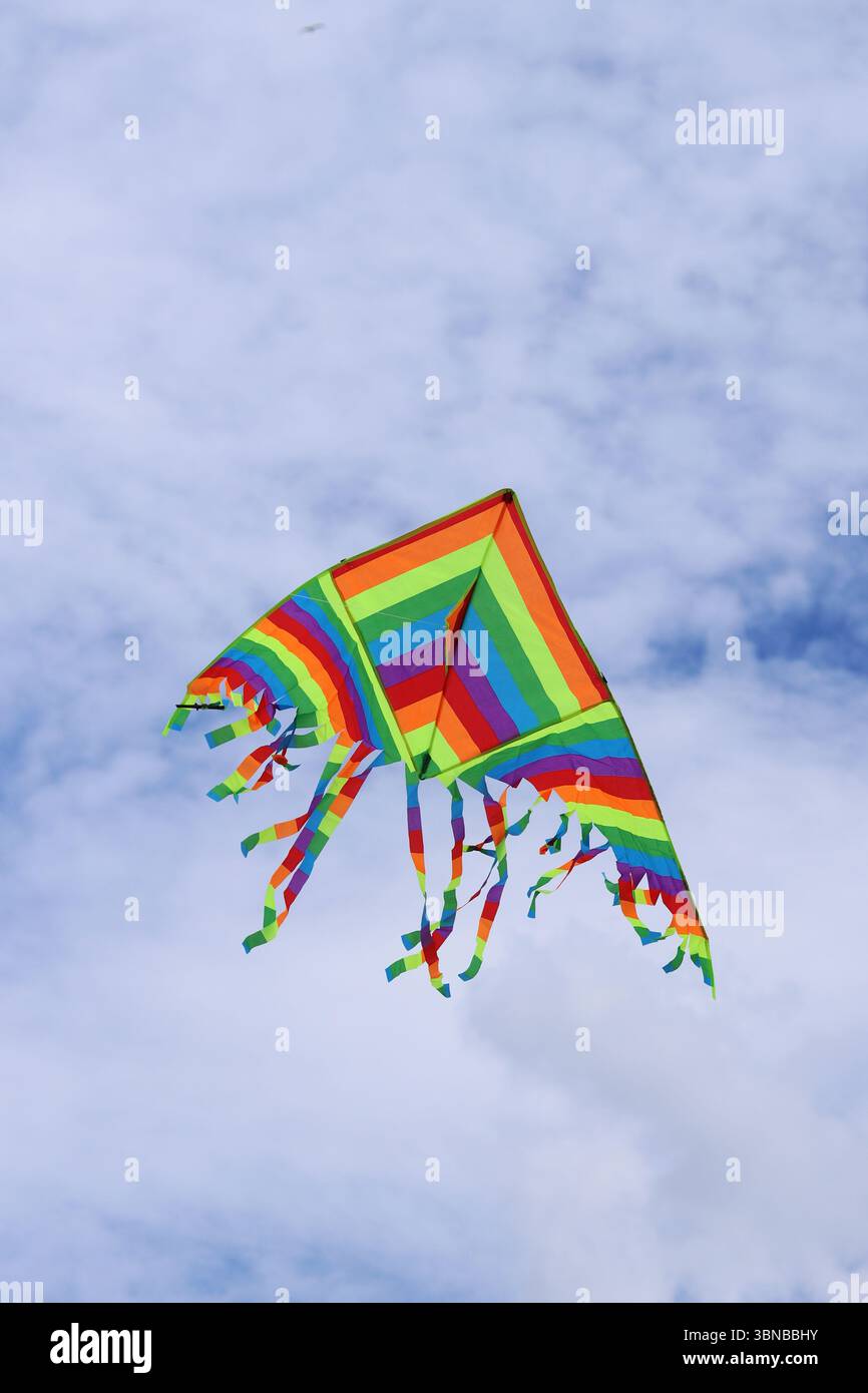 Heller Drachen vor dem bewölkten Himmel. Spielzeug für Kinder und Erwachsene. Outdoor-Aktivitäten. Bunte Drachenfliegen am Himmel, windiges Wetter. Wolkenlose Stimmung Stockfoto