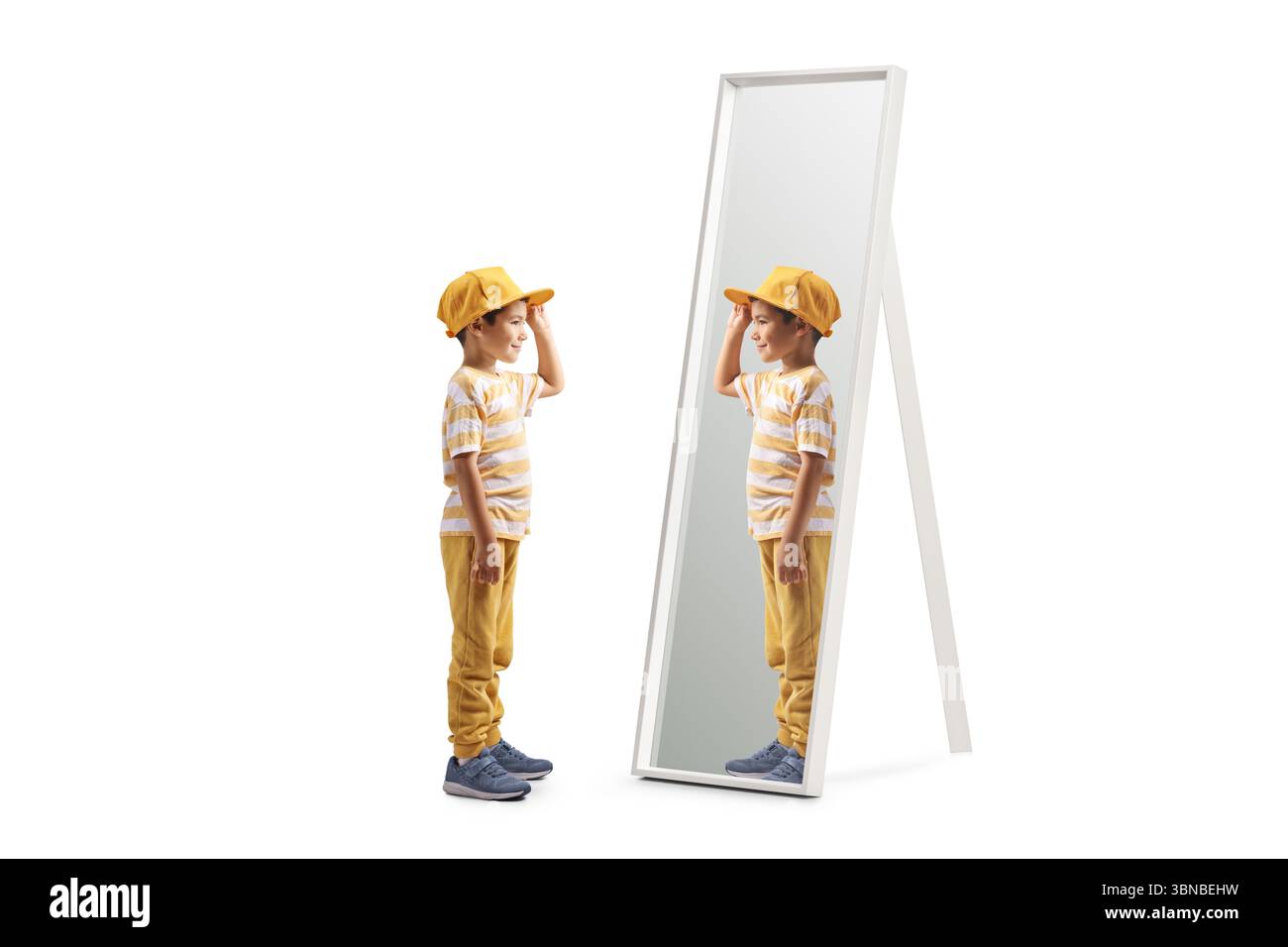 Profilaufnahme eines Jungen mit gelber Kappe, der vor einem Spiegel steht, isoliert auf weißem Hintergrund Stockfoto