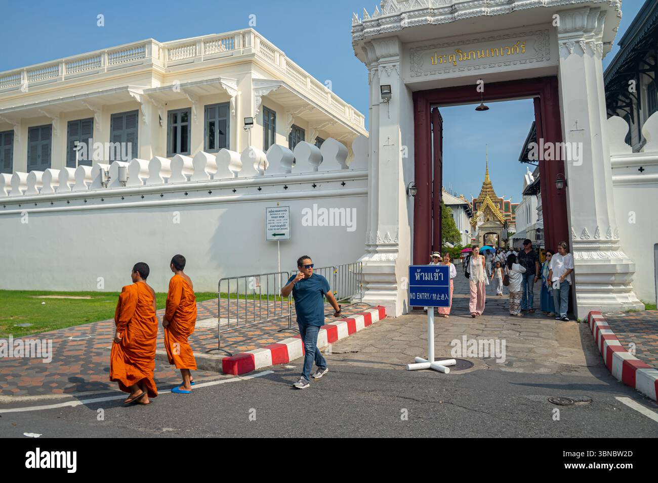 Touristen verlassen sich, Mönche gehen an einem Tor an einem historischen Grand Palace, Königspalast Komplex in Bangkok, Thailand vorbei. Stockfoto