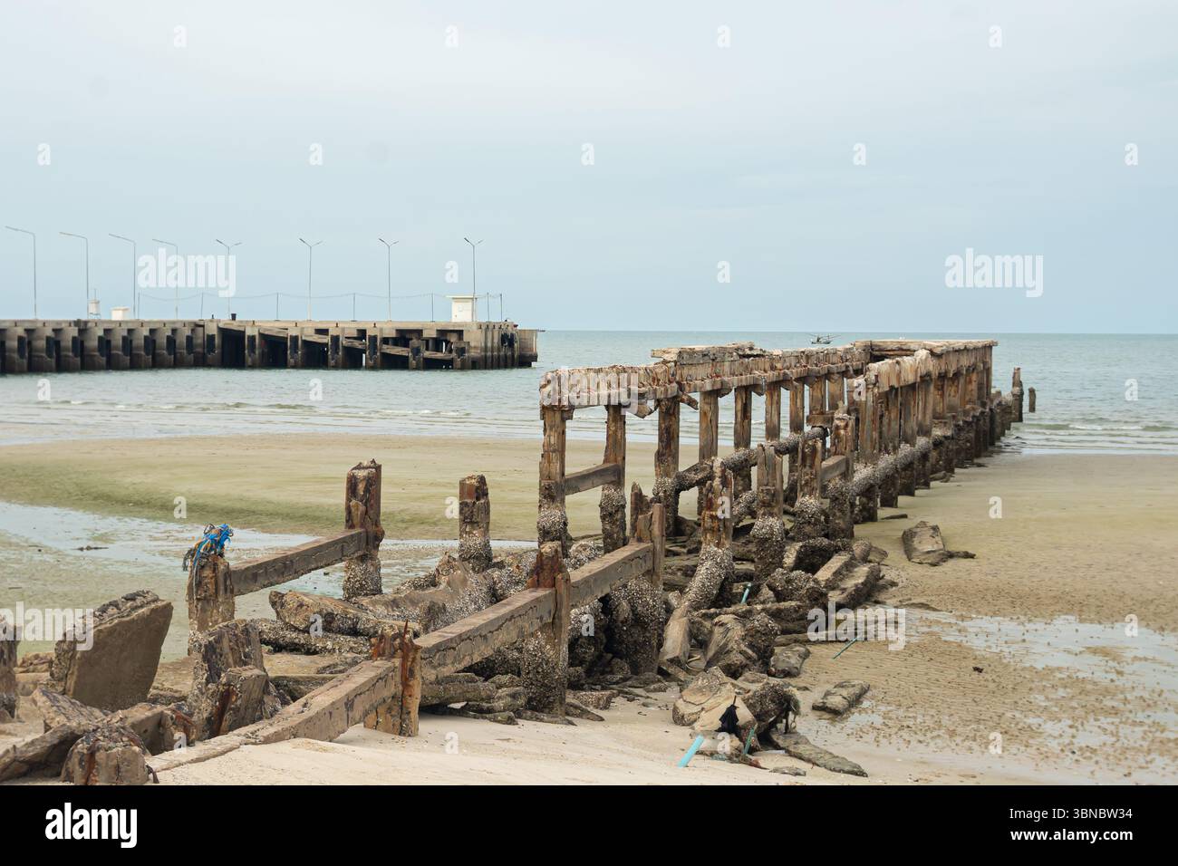 Ein alter, baufälliger Pier erstreckt sich bis ins Wasser an einem trüben Strand, Hua hin Resort, Thailand Stockfoto
