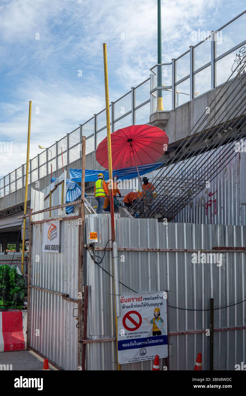 Arbeiter unter Schirm, Baustelle mit Barrieren neben einem traditionellen thailändischen Gebäude, unter der Autobahn, Bangkok Noi, Thailand Stockfoto