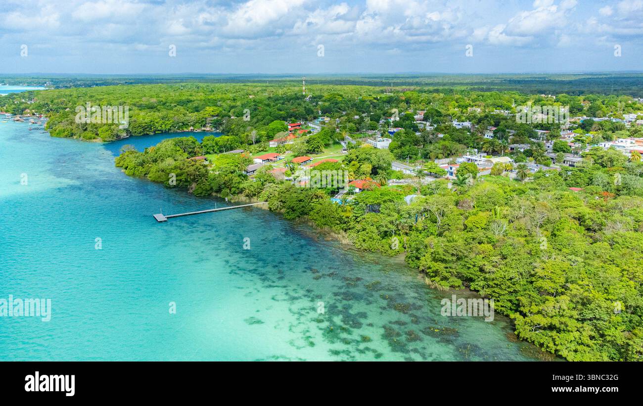 Bacalar, Mexiko, Quintana Roo, grünes Gewässer mit einer kleinen Stadt am Ufer. Das Wasser ist ruhig und der Himmel ist klar Stockfoto