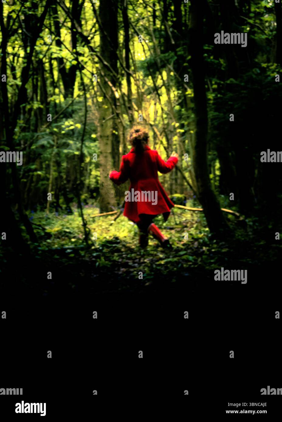 Eine Person in rotem Mantel rennt durch einen Wald. Stockfoto