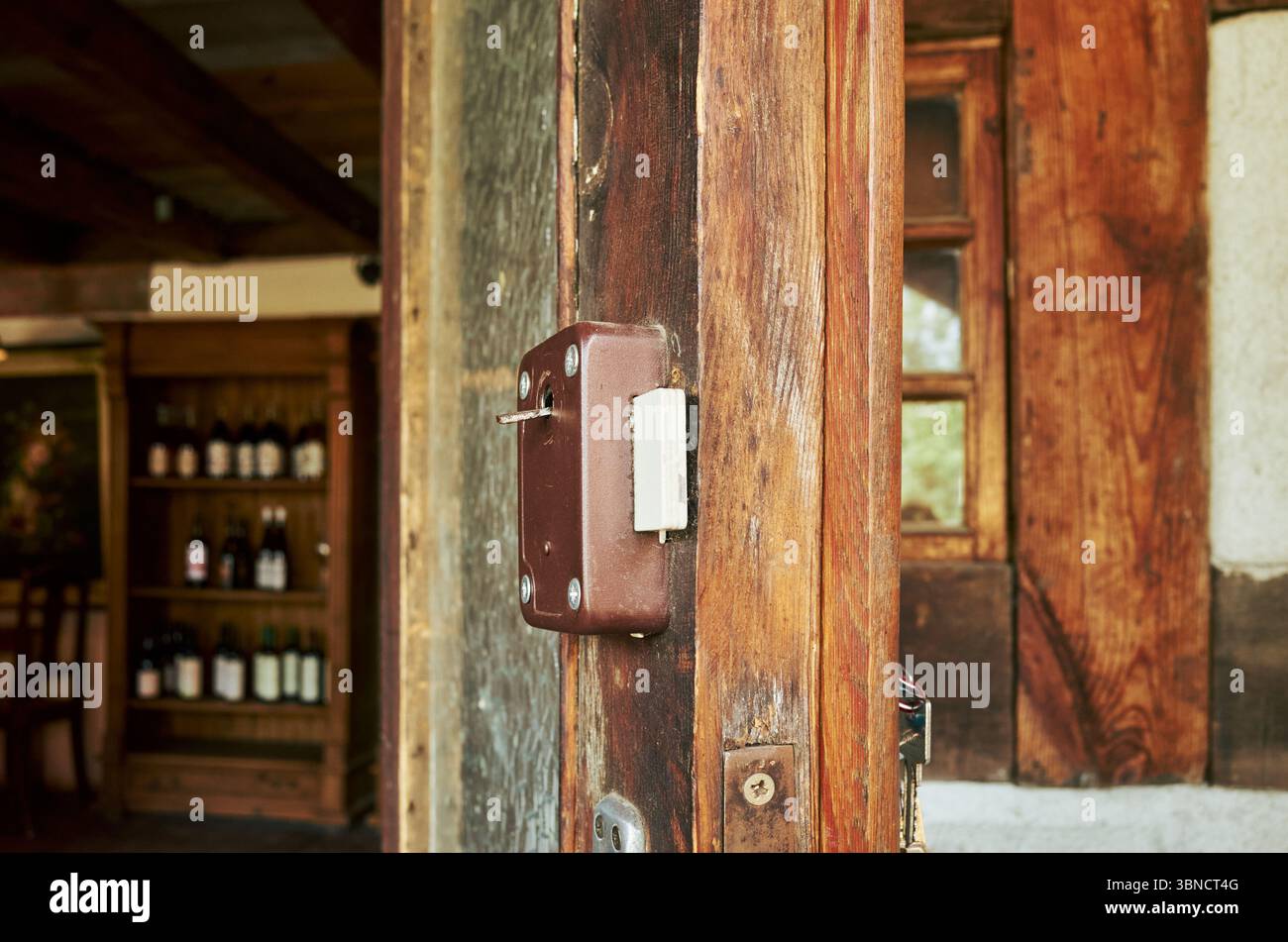 Holztür mit einem Schloss drauf. Die Tür ist vor einem Weinkeller. Der Weinkeller hat viele Flaschen drauf Stockfoto