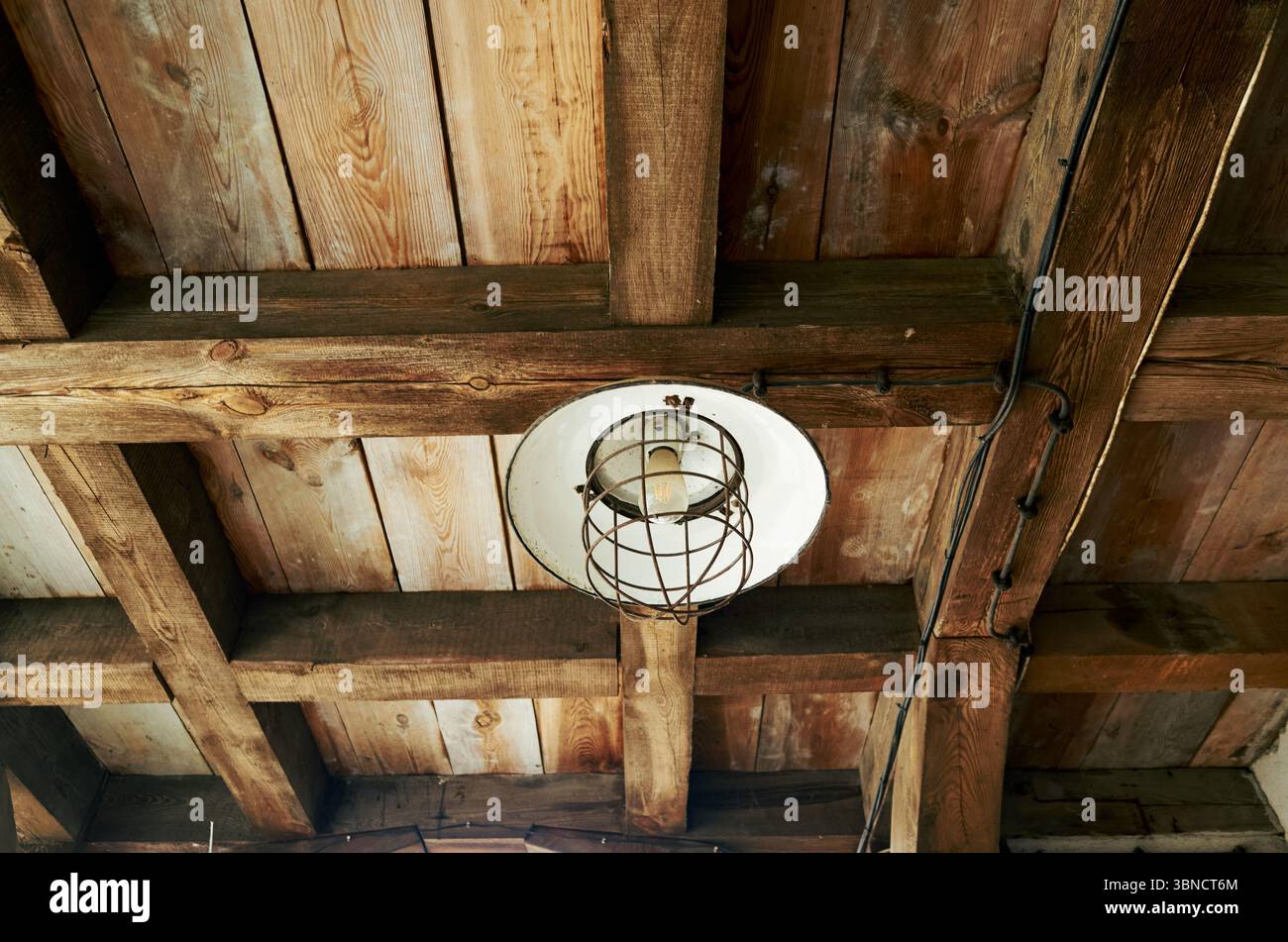 In einem Holzraum hängt die Leuchte von der Decke. Die Leuchte ist eine Laterne mit einem weißen Schatten. Das Zimmer hat eine rustikale Atmosphäre, mit Holzbalken Stockfoto