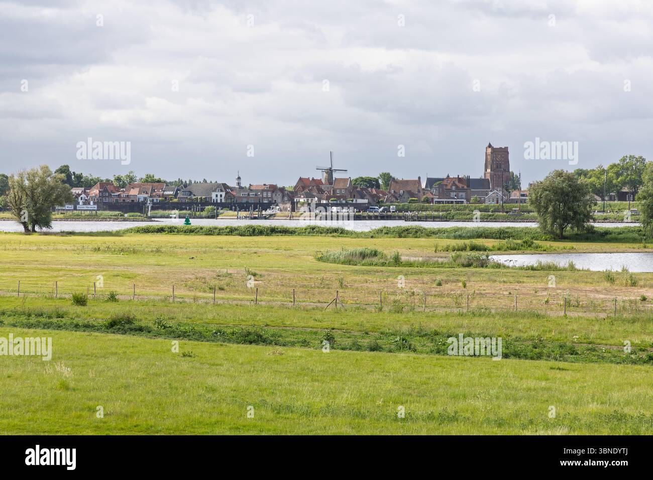 Ein wunderschöner Panoramablick auf die historische Stadt Woudrichem, Niederlande, mit ihrer berühmten Kirche und Windmühle, eingebettet von einem breiten Fluss und üppig Stockfoto