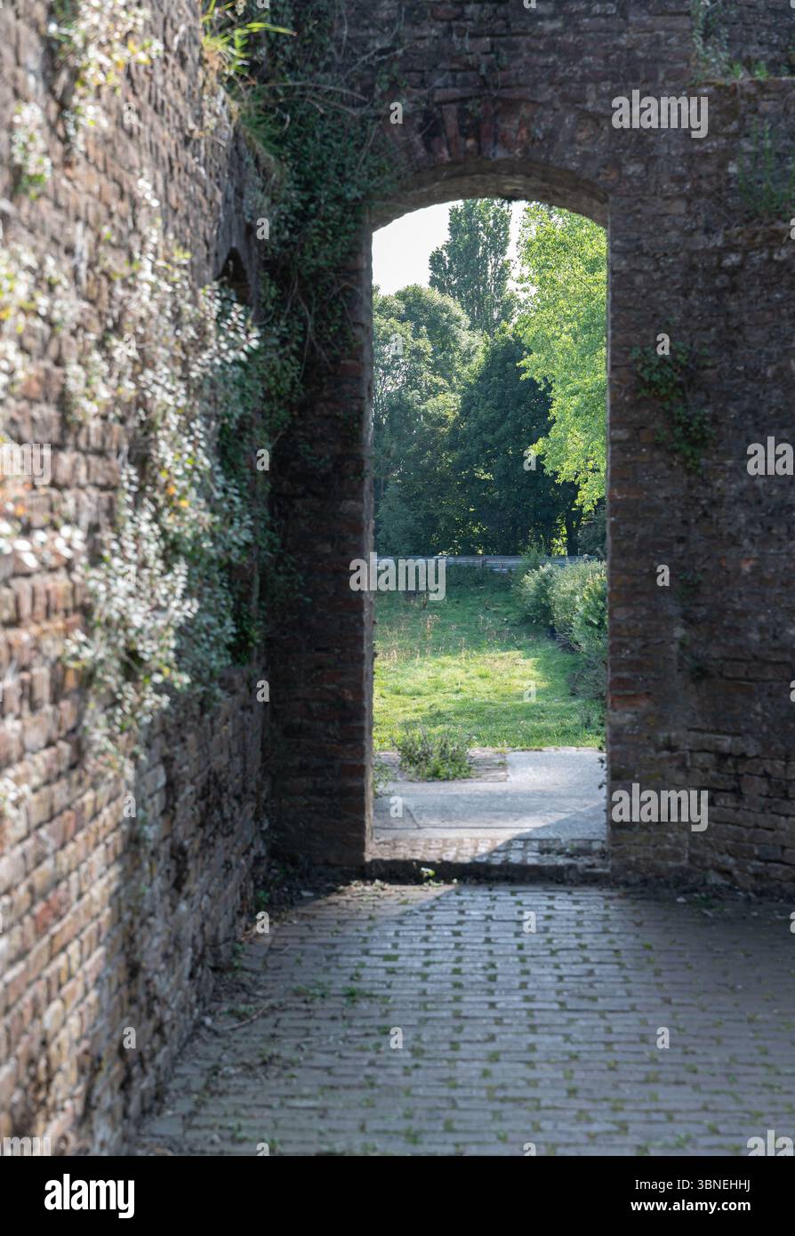 Eine elegante Bogenöffnung offenbart eine friedliche und ruhige grüne Landschaft, kunstvoll eingerahmt von alten Ziegelmauern Stockfoto