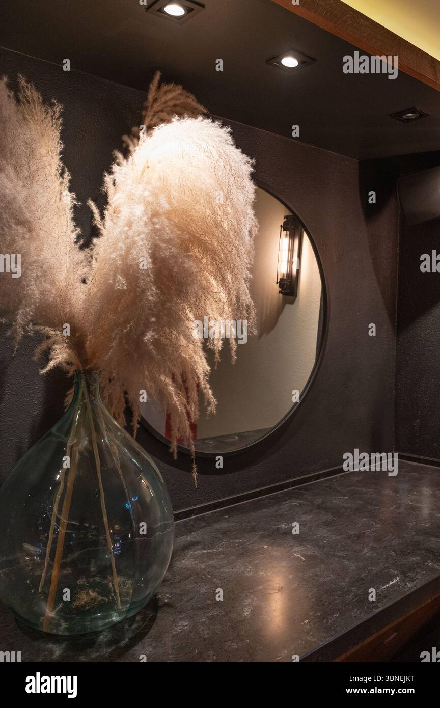 Das stilvolle Innendesign bietet wunderschönes Pampas-Gras, das elegant in einer Vase neben einem schicken runden Spiegel angeordnet ist Stockfoto