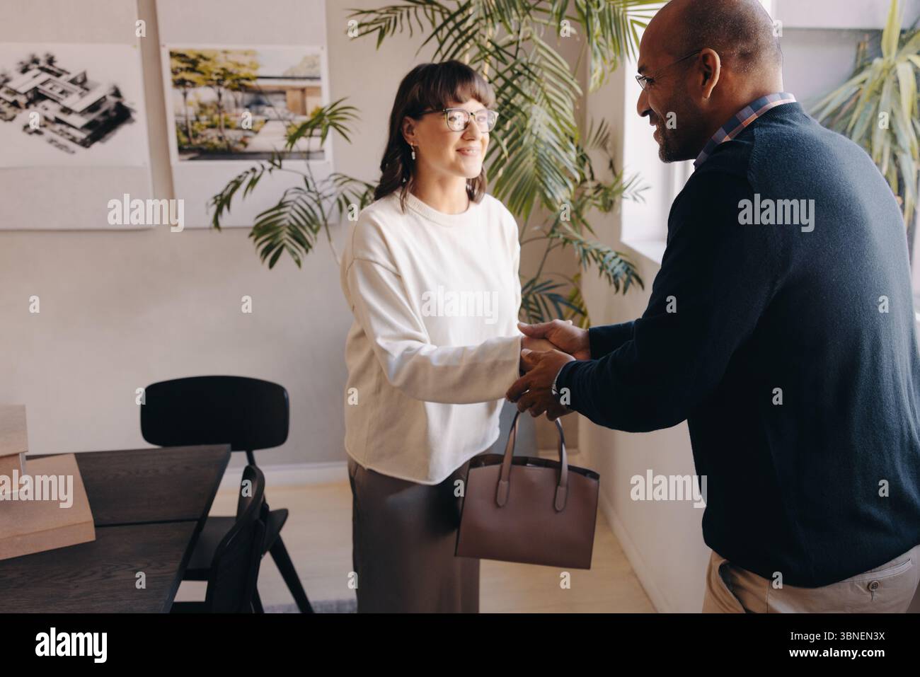 Ein Geschäftstreffen, bei dem sich zwei Personen in einem freundlichen Handschlag beteiligen, das Vertrauen und erfolgreiche Zusammenarbeit symbolisiert und in einem modernen Bürobereich stattfindet Stockfoto