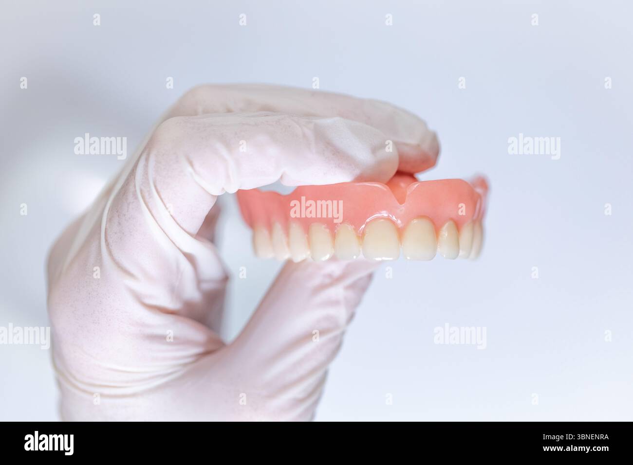 Gebrauchte obere Prothese, die in einer Hand mit Handschuhen detailliert dargestellt und mit hellem Licht beleuchtet wird, zeigt Verschleiß, Flecken und klinische Authentizität. Stockfoto