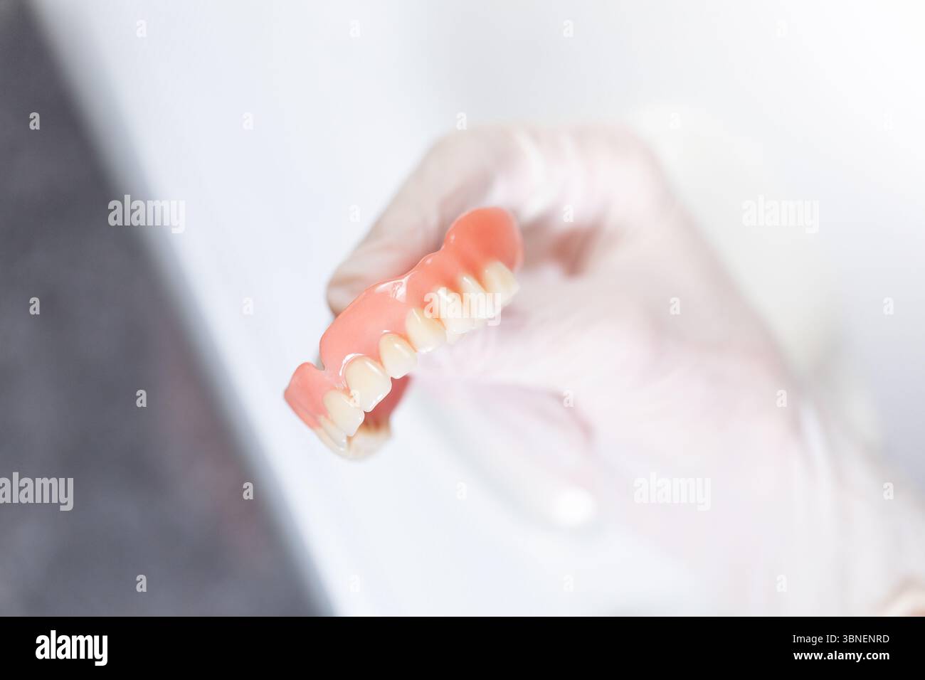 Nahaufnahme eines medizinischen Handschuhs mit realistischer Oberprothese in sauberer, weißer Beleuchtung, die die Handhabung alter Zahnersatzprothesen veranschaulicht. Stockfoto
