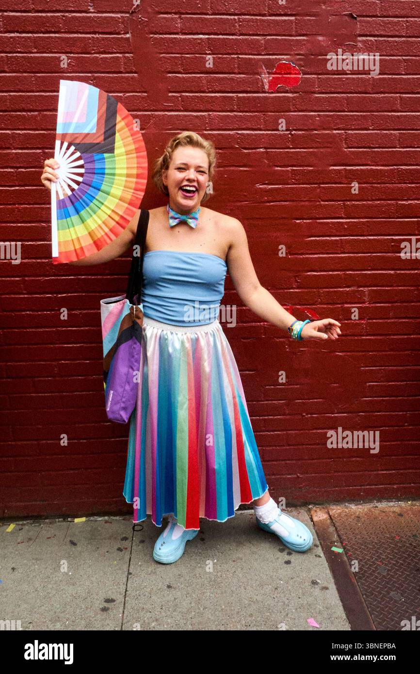 New York, NY, USA - 30. Juni 2024 Frau mit großem Regenbogenhandventilator vor der roten Ziegelwand Stockfoto