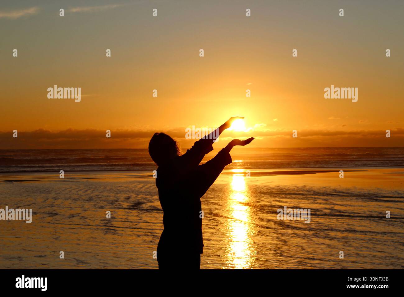 Frau hält Sonne in der Hand, magischer Sonnenuntergang am Karioitahi Beach, alles ist möglich Stockfoto
