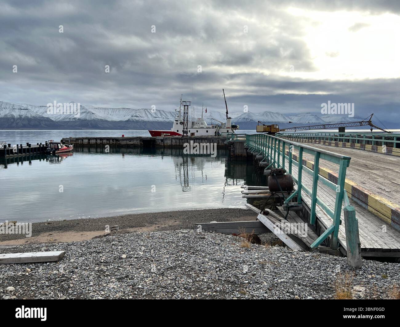 Eine ruhige Küstenszene mit Booten, einem Pier und fernen Bergen unter einem bewölkten Himmel in Pyramiden, Svalbard - Smartphone-aufgenommenes Stockfoto