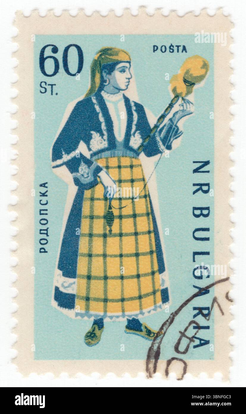 BULGARIEN — 28. Januar 1961: 60 stotinki grünblauer, preußischer blauer und gelber Poststempel mit den regionalen Trachten von Rhodopen. Eine Volkstracht (auch nationale, traditionelle Kleidung oder Insignien). Eine Volkstracht (auch regionale Tracht, nationale Tracht, traditionelle Kleidung oder traditionelle Insignien) drückt eine Identität durch Tracht aus, die normalerweise mit einem geografischen Gebiet oder einer Zeitspanne in der Geschichte verbunden ist. Sie kann auch den sozialen, ehelichen oder religiösen Status anzeigen. Wenn das Kostüm verwendet wird, um die Kultur oder Identität einer bestimmten ethnischen Gruppe zu repräsentieren, wird es normalerweise als ethnische Gruppe bezeichnet Stockfoto