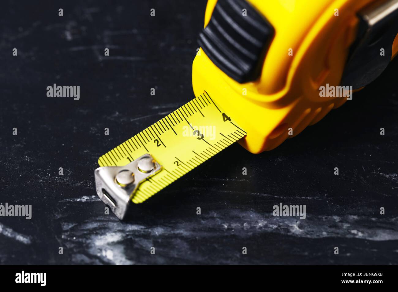 Nahaufnahme des gelben Maßbandes. DIY-Werkzeug auf dunklem Schieferhintergrund. Einziehbares Messgerät für Bau- und Renovierungsarbeiten. Stockfoto