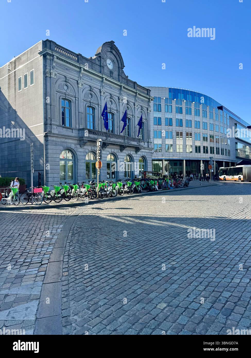 Neoklassizistisches Gebäude mit EU-Flaggen und einer Reihe von gemeinsamen Fahrrädern, das auf einem Kopfsteinpflasterplatz in Brüssel, Belgien, geparkt ist. - Smartphone-aufgenommenes Stockfoto