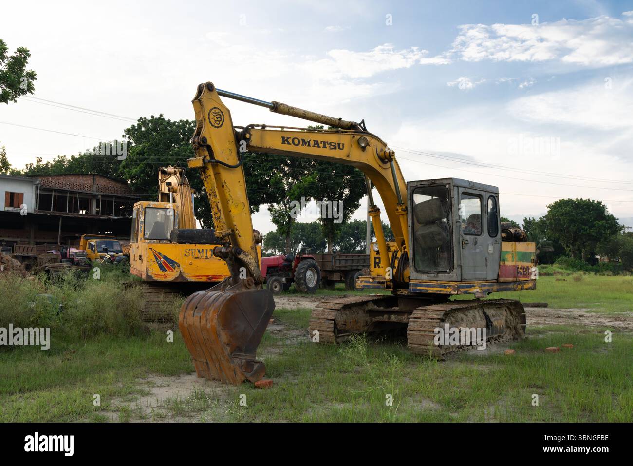 Ein gelber und rostiger Bagger auf einem grünen Feld Stockfoto