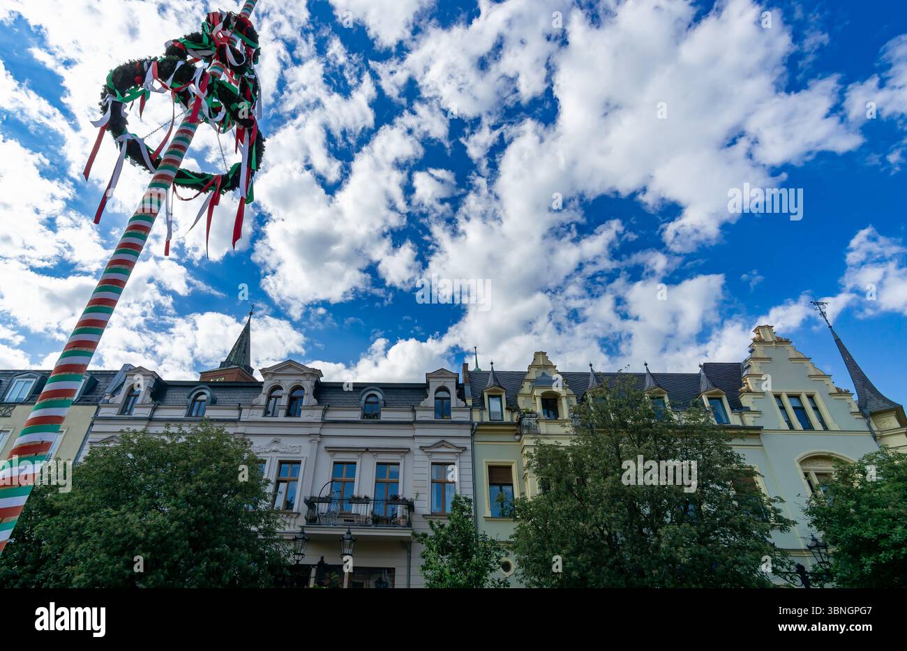 Traditionelles Maypole und historische Fassaden am Rathausplatz in Bernau bei Berlin, Deutschland, unter einem dramatischen blauen Himmel. Stockfoto