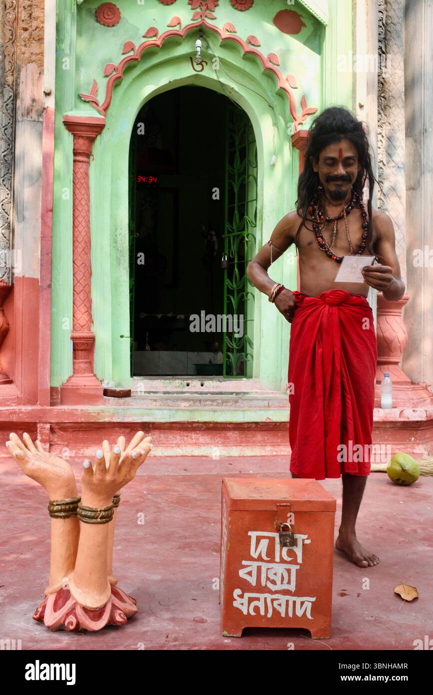 Sadhu auf dem Gelände von Natore Rajbari, Bangladesch, neben einer Spendenkiste und symbolischen Handskulpturen. Stockfoto