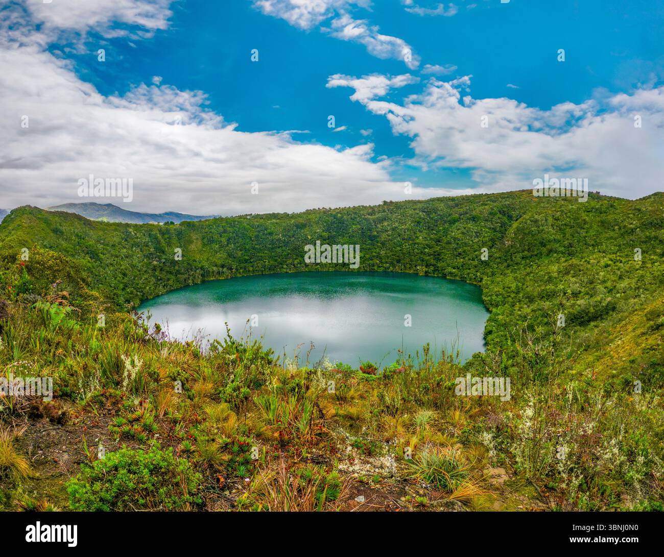 Atemberaubende Aussicht auf Laguna de Guatavita, umgeben von üppigem Grün und blauem Himmel in Guatavita, Cundinamarca, Kolumbien. Stockfoto