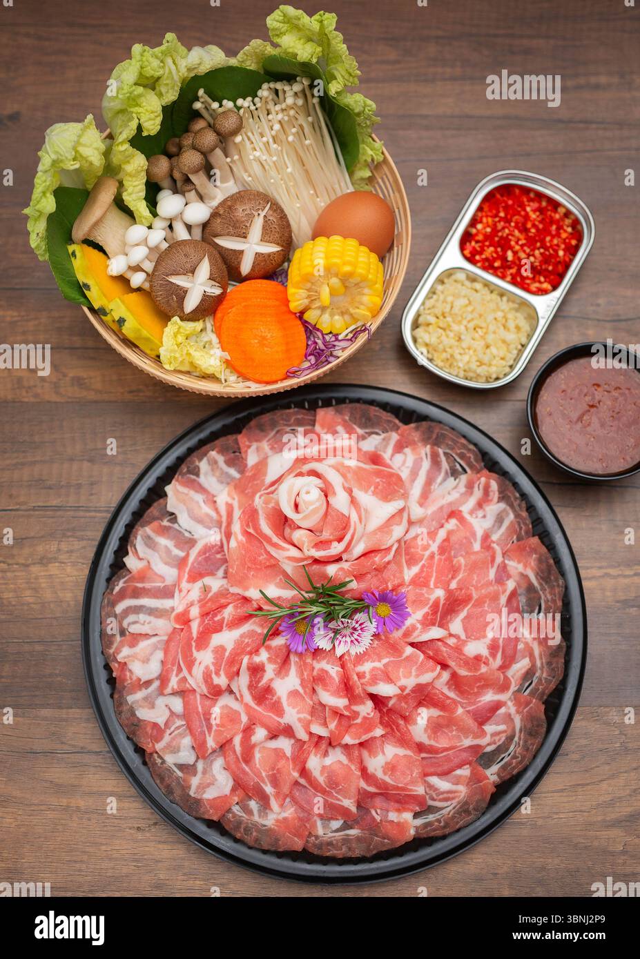Ein wunderschön gestaltetes japanisches Hot Pot (Shabu Shabu) Set mit dünn geschnittenem Schweinefleisch, das in Blütenform auf einem schwarzen Tablett angeordnet ist, umgeben von Stockfoto
