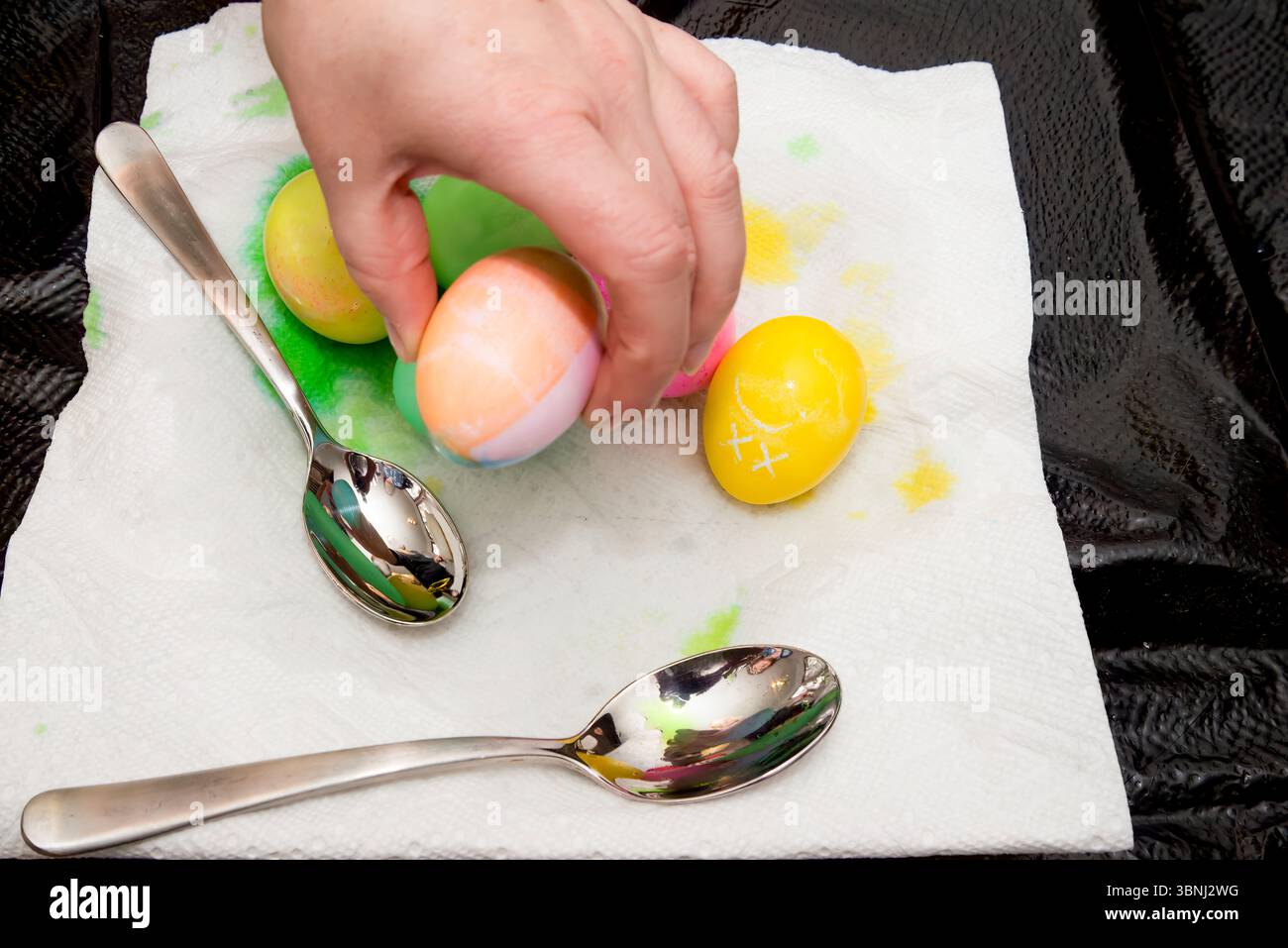 Eine Hand, die ein Osterei aus einem Haufen frisch gefärbter Eier aufnimmt. Stockfoto