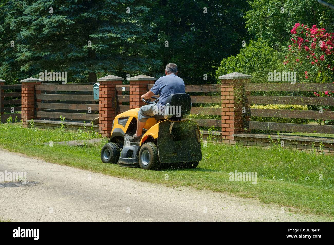 Mann, der mit einem Aufsitzmäher vor dem Haus Grasränder auf der Landstraße zala County ungarn schneidet Stockfoto