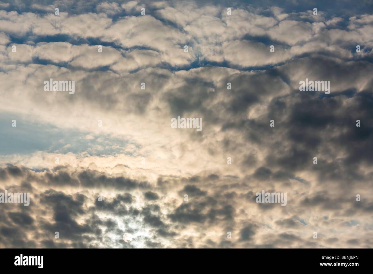 Die Sonne scheint schwach durch dicke, strukturierte Wolken und schafft einen dramatischen und stimmungsvollen Himmel mit kontrastierenden Licht und Schatten. Stockfoto Die Sonne scheint schwach durch dicke, strukturierte Wolken und schafft einen dramatischen und stimmungsvollen Himmel mit kontrastierenden Licht und Schatten. Stockfoto