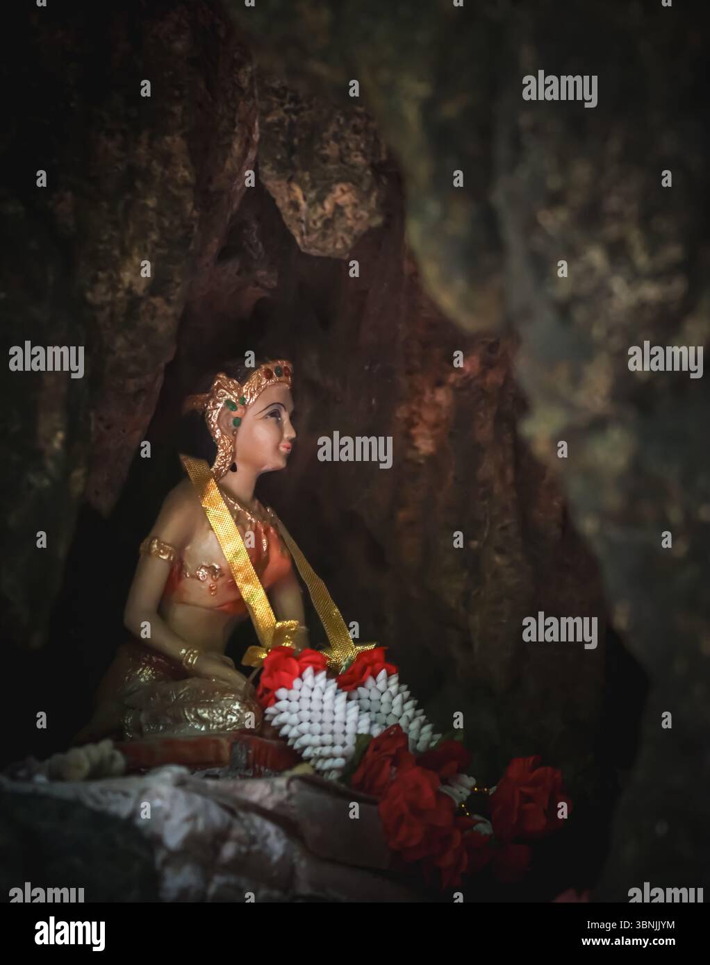 Eine Statue einer weiblichen Gottheit oder Prinzessin in traditioneller thailändischer Kleidung befindet sich in einem kleinen, dunklen Höhlenschrein. Die Figur ist mit einem Kopfschmuck verziert. Stockfoto