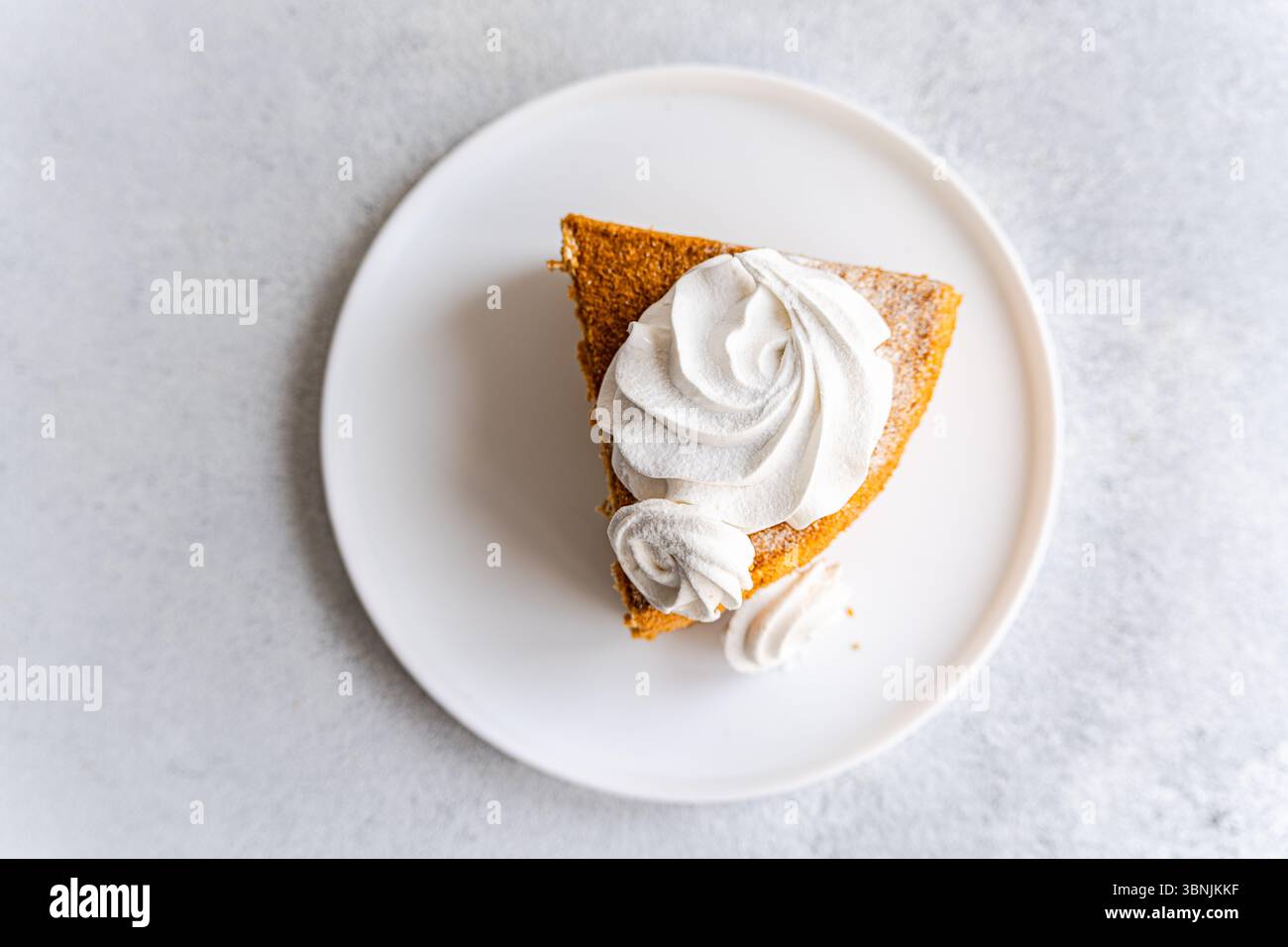 Von oben sitzt ein Stück hausgemachter Honigkuchen mit einem Schuss Vanille zephyr elegant auf einem weißen Teller. Begleitet von einem Klecks cremiger Sou Stockfoto