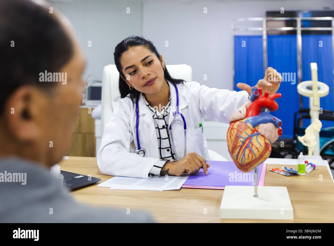 Eine fürsorgliche junge Ärztin betreut einen älteren männlichen Patienten in einem warmen und professionellen lateinamerikanischen Krankenhaus-Setting und zeigt aufmerksame Heilung Stockfoto