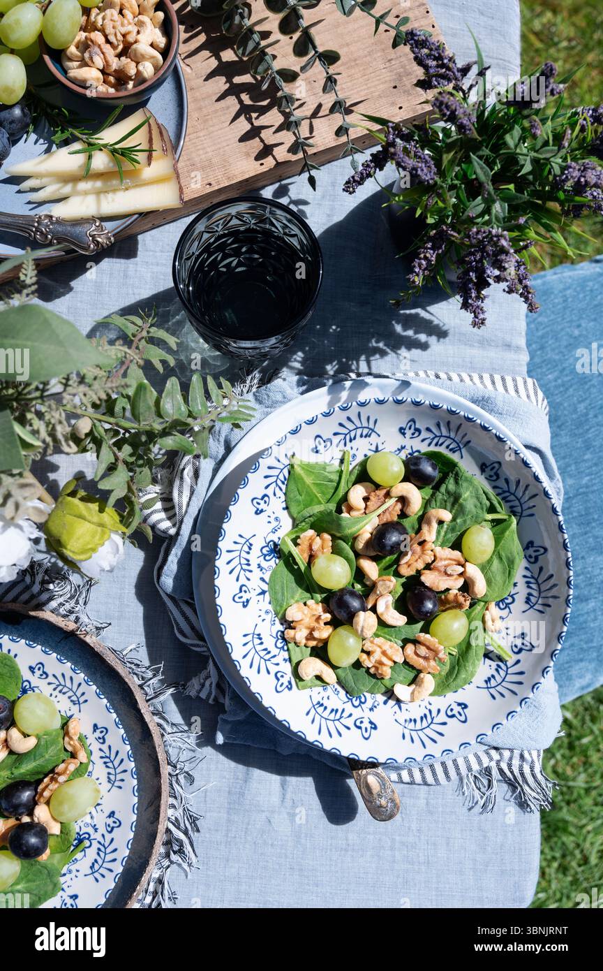 Ein erfrischender Salat aus Lammsalat, Trauben, Cashews und Walnüssen auf einem gemusterten Teller. Im Freien unter der Sonne, diese Mahlzeit A Stockfoto