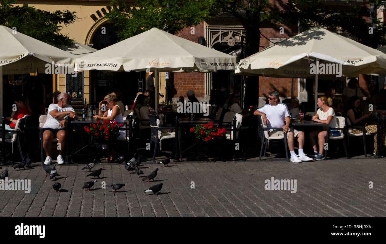 Straßenszene mit Touristen, die im Freien in der Altstadt von Kraków speisen; die Gäste entspannen sich in einem Restaurant im Freien. Stockfoto