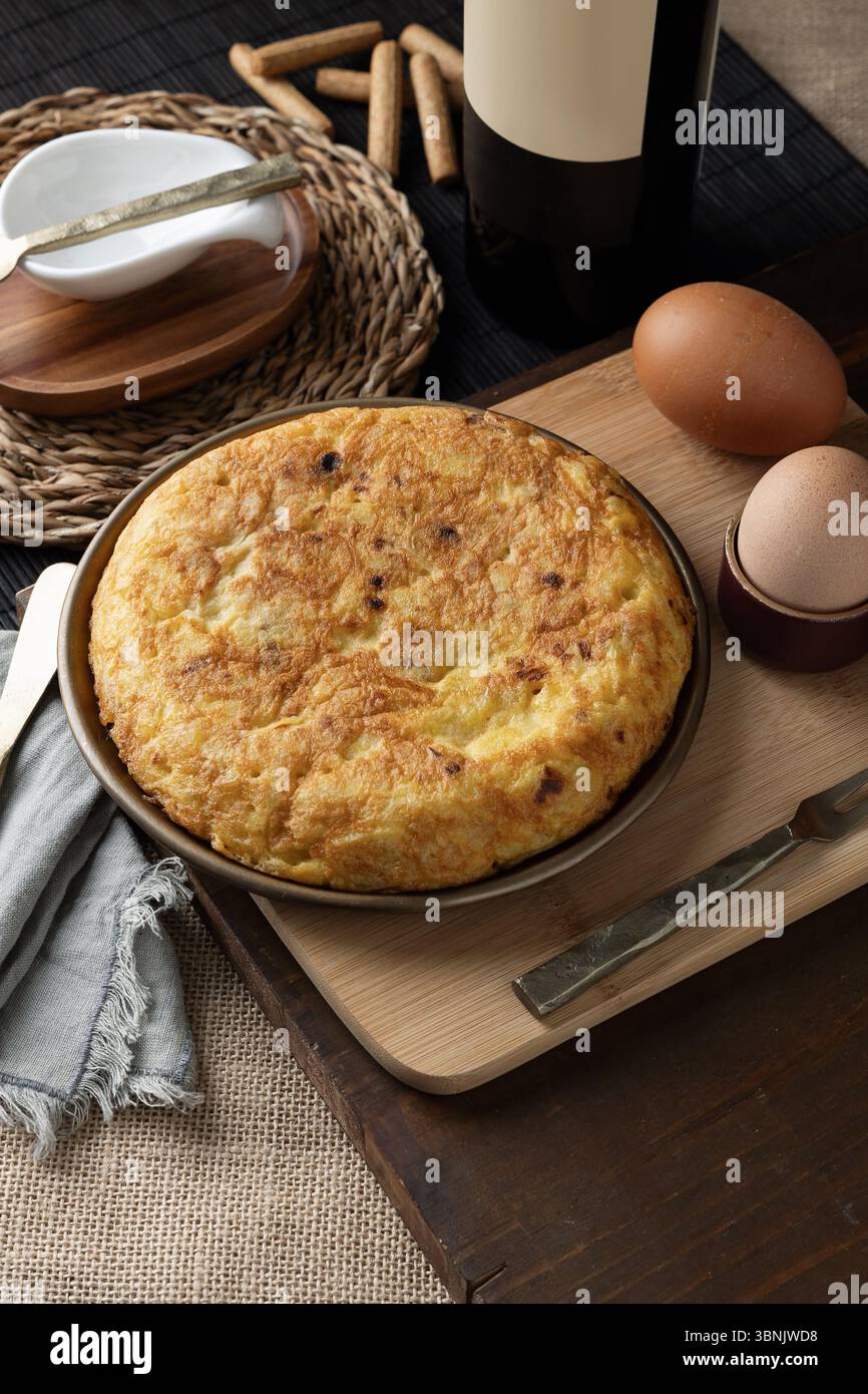 Ein köstliches spanisches Omelett wird auf einem rustikalen Holztisch präsentiert, umgeben von frischen Zutaten. Es ist ein typisches Gericht der spanischen Küche. Stockfoto