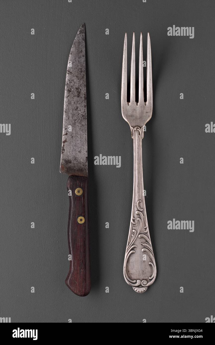 Ein antikes Messer- und Gabelset mit komplizierten Designs auf grauem Hintergrund. Die Vintage-Utensilien sind mit Holz- und Silberdetails versehen Stockfoto